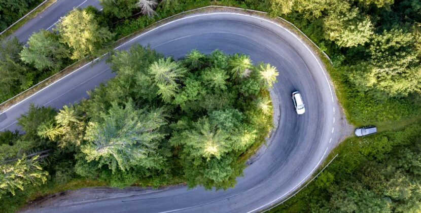 Aerial view of winding road in high mountain pass trough dense green pine woods.