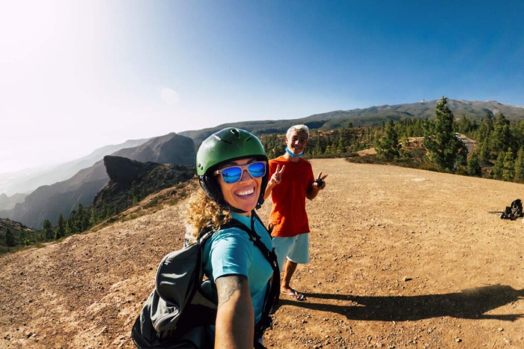 Boy posing with mother taking selfie on mountain landscape. Happy woman traveler in helmet and sunglasses taking selfie with her teenage son posing on mountain on a bright sunny day