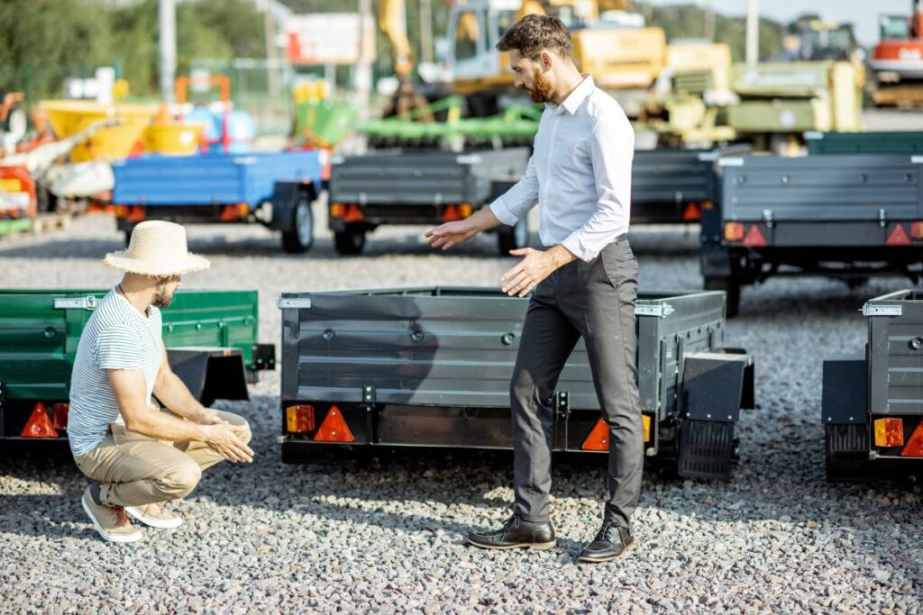 Agronomist with salesman choosing a new farm truck trailer, standing on the open ground of the agricultural shop