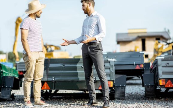Agronomist with salesman choosing a new farm truck trailer, standing on the open ground of the agricultural shop