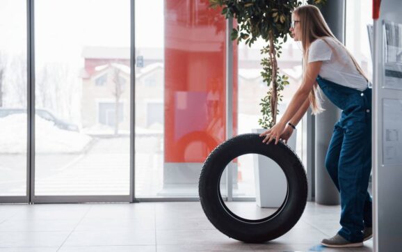 Cold weather outside. Woman walks with brand new wheel to the car. Conception of repair