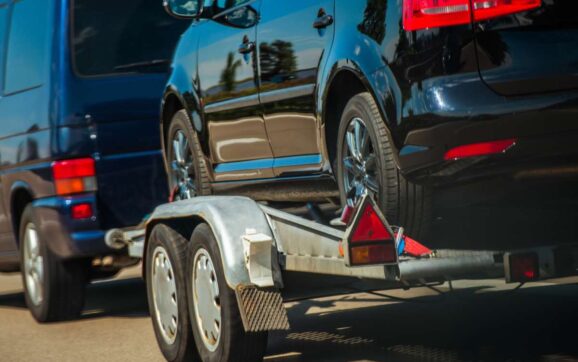 Used Cars Importing in European Union. Van Pulling Trailer with Damaged Pre Owned Vehicle For Sale in Other Country.