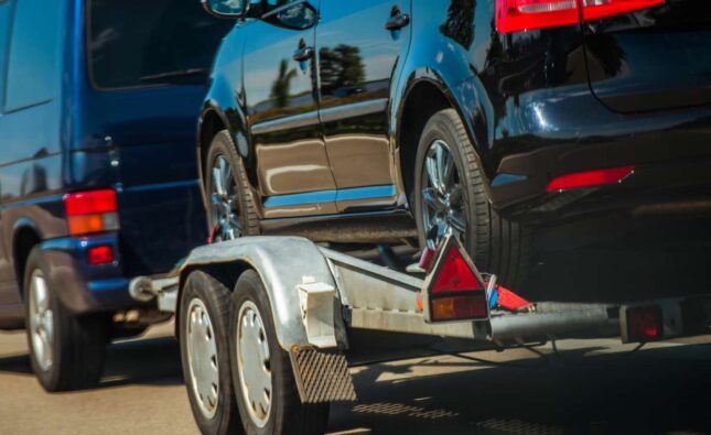 Used Cars Importing in European Union. Van Pulling Trailer with Damaged Pre Owned Vehicle For Sale in Other Country.